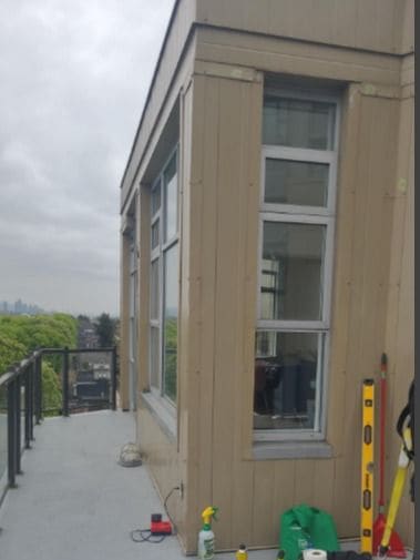 An upper-floor balcony with a grey deck surface, a level, a spray bottle and other tools set along the wall