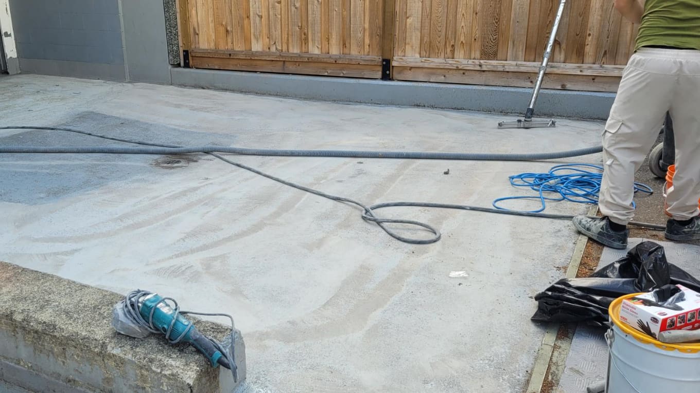 A concrete deck being mechanically ground back to sound substrate, grinder and vacuum hose in frame